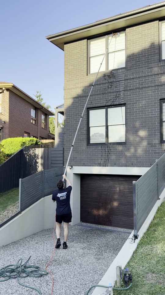 Squeegee Boys crew member cleaning a second-storey window with a water-fed pole